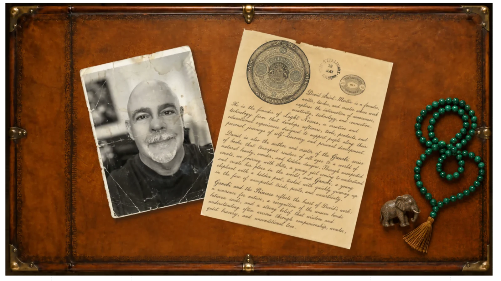 An antique leather desktop displaying David Saint-Martin's photograph, handwritten biography, green mala beads, and a small elephant